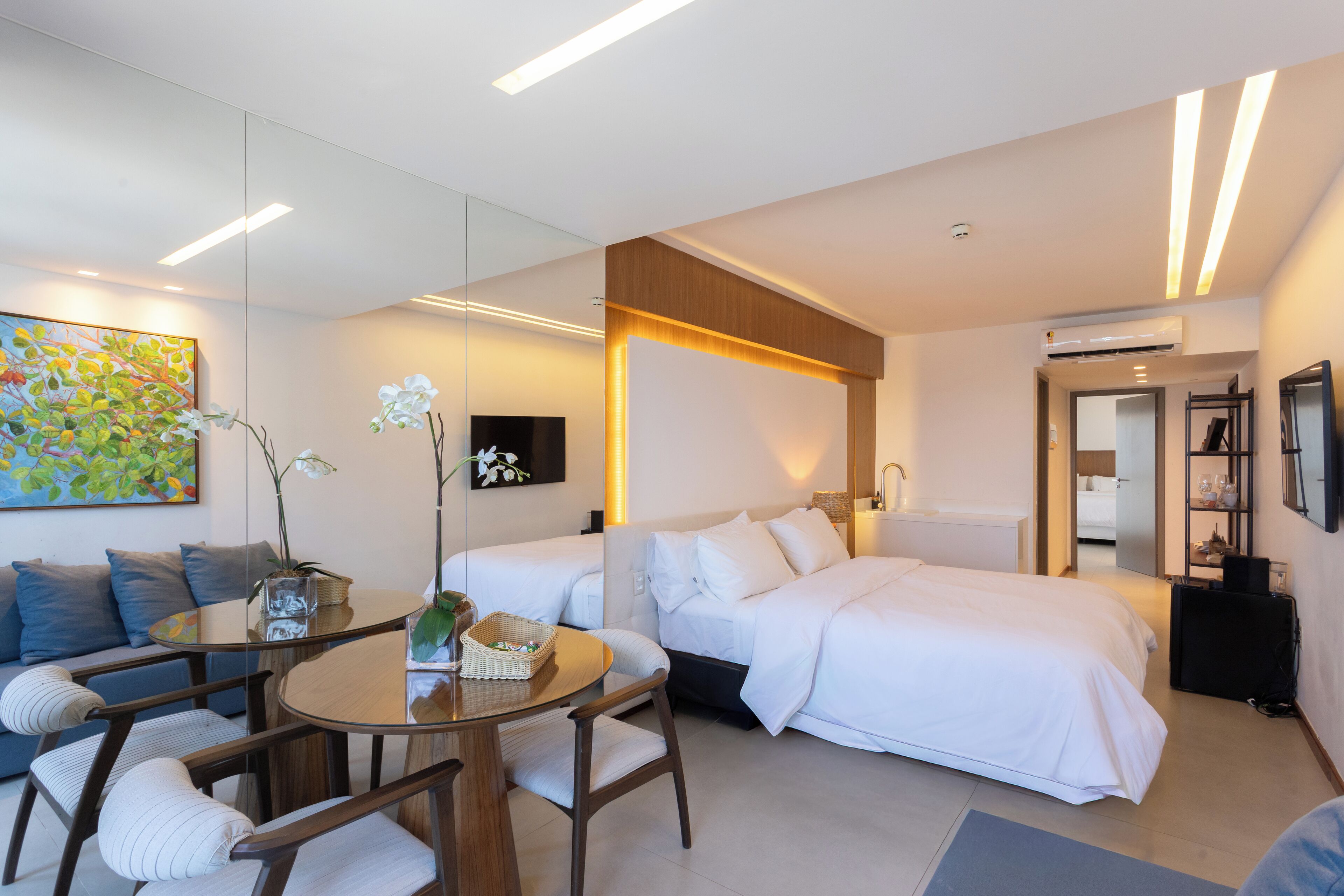 A modern hotel room with a bed, a sofa, a dining table, and a TV.