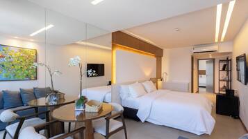 A modern hotel room with a bed, a sofa, a dining table, and a TV.