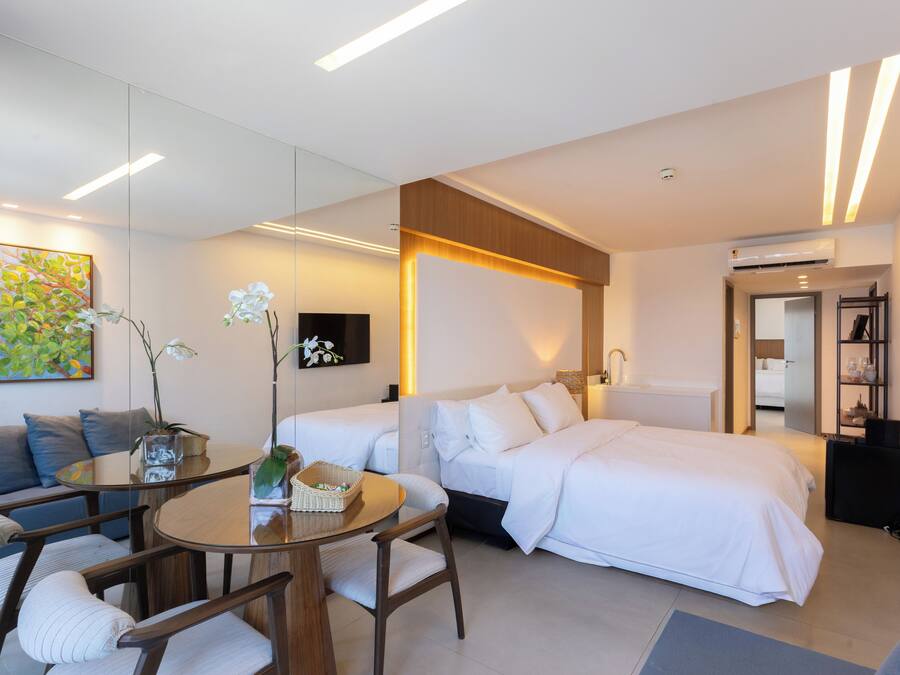 A modern hotel room with a bed, a sofa, a dining table, and a TV.