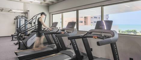 A gym with treadmills, a weight machine, and a large window with a view of buildings and the sky.