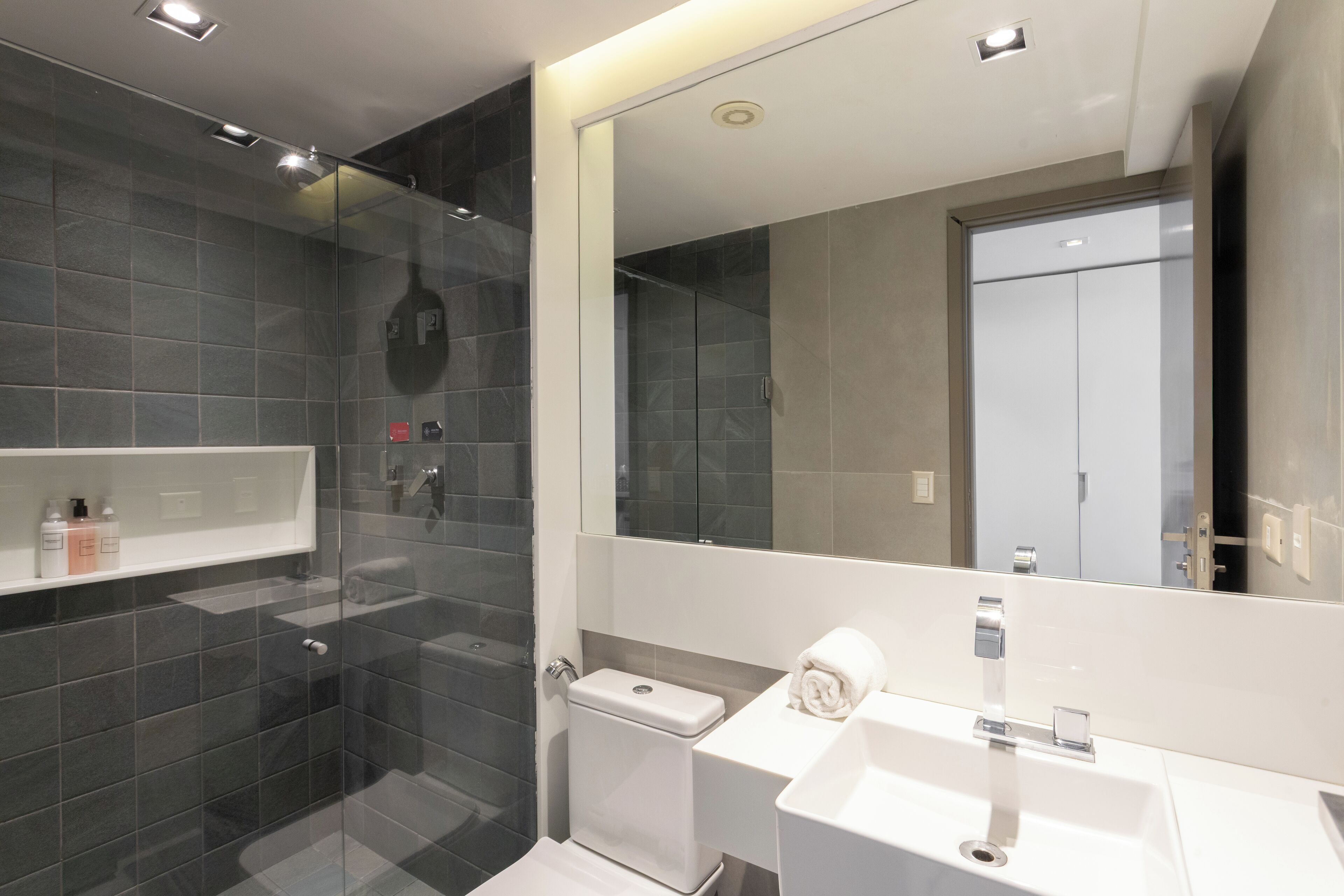 Un baño moderno con ducha envuelta en vidrio, un lavamanos blanco y un espejo grande.