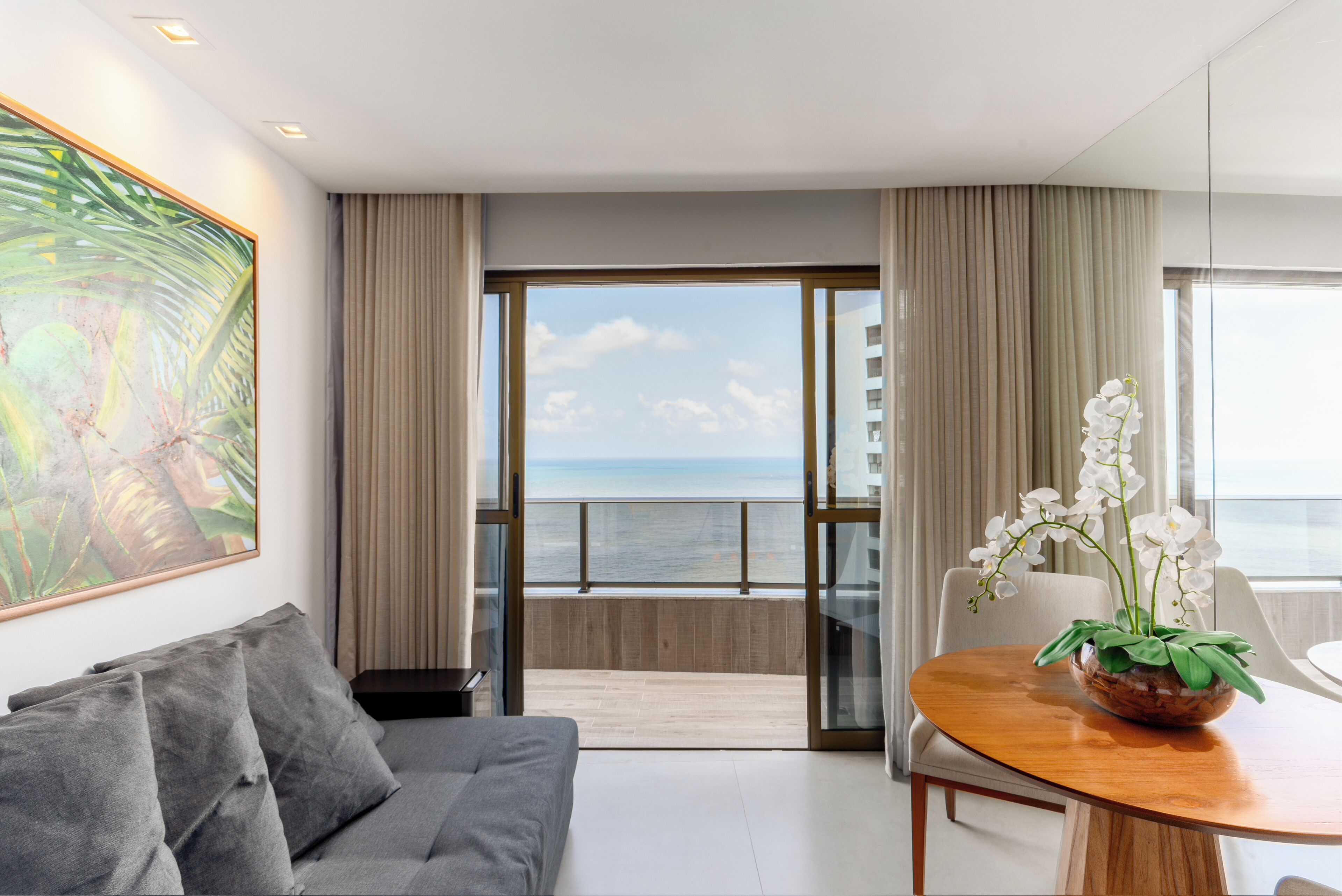 Una habitación de hotel moderna con balcón, zona de comedor y un cuadro grande.
