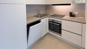 A compact kitchen with white cabinets, a stainless steel sink, and a built-in oven. - Elegant and Luminous Apartment With Terrace (San Michele al Tagliamento)