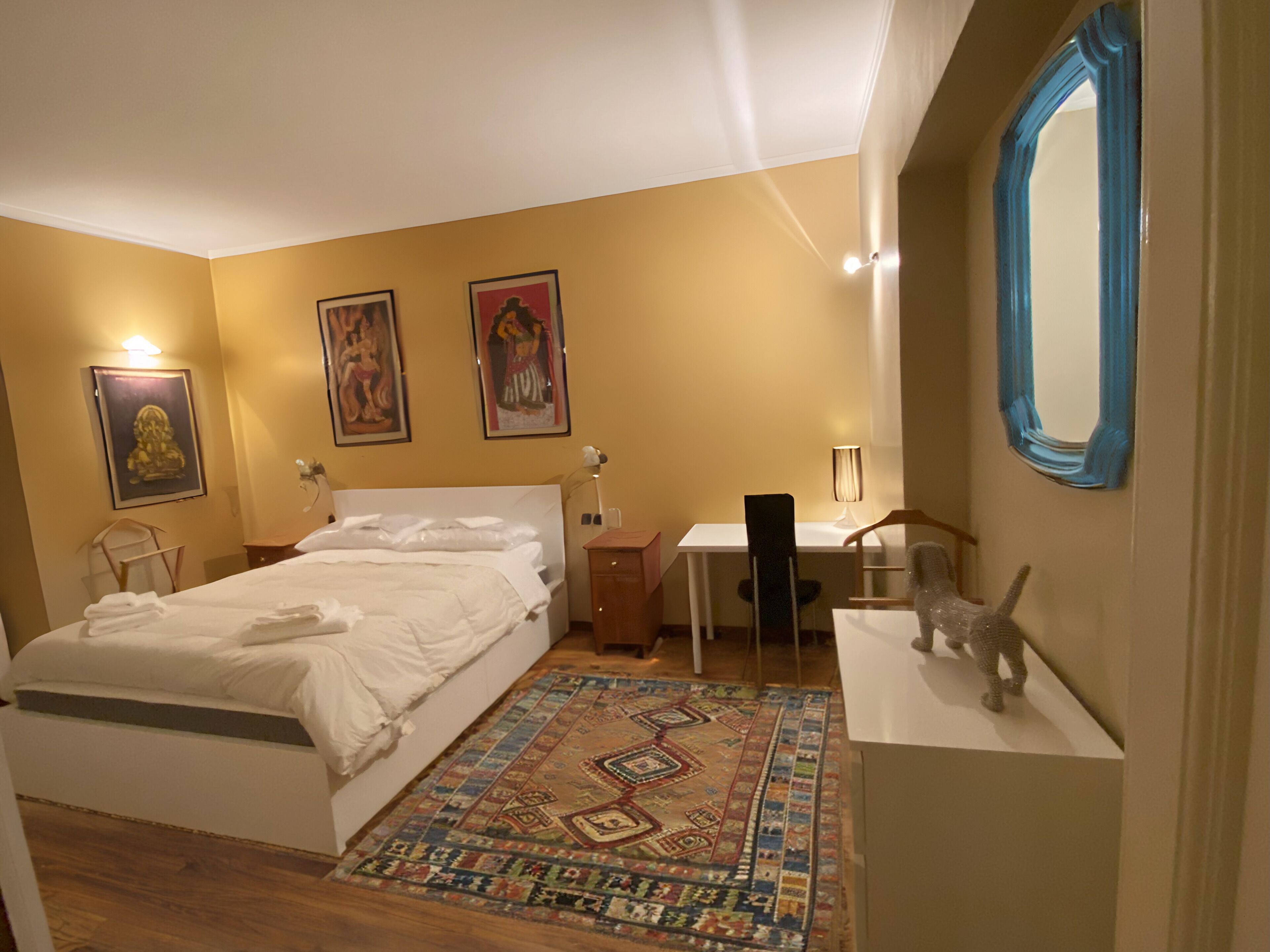 A bedroom with a bed, desk, chair, and a mirror.