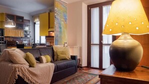 Uma sala de estar aconchegante com um sofá escuro, um tapete estampado e uma luminária grande sobre uma mesa de madeira.
