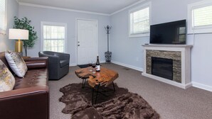 A living room with a brown leather sofa, a wooden coffee table, and a fur rug. There is a fireplace, a television, and a coat rack. - Peaceful 1BR Apartment for Extended Stays in Huntersville (Huntersville)