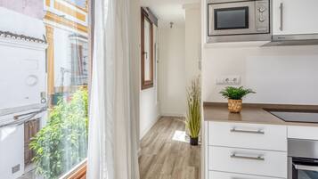 A modern kitchen with white cabinets, a microwave, and a stove. There is a potted plant on the counter and a window with curtains.