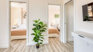 Een hotelkamer met een bed, nachtkastje, lamp en een plant in pot. Er zijn twee deuren die naar andere kamers leiden.