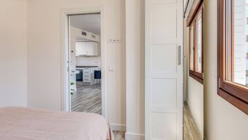 A bedroom with a bed, a door leading to a kitchen, and a window with blinds.