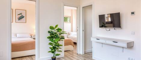 A modern hotel room with a bed, bedside table, potted plant, and a mounted TV.
