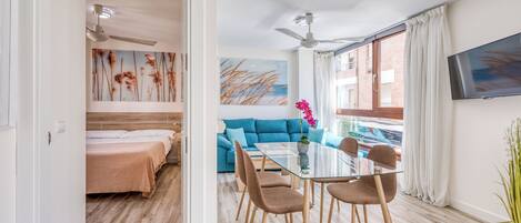 A modern hotel room with a dining area, a sofa, and a TV.