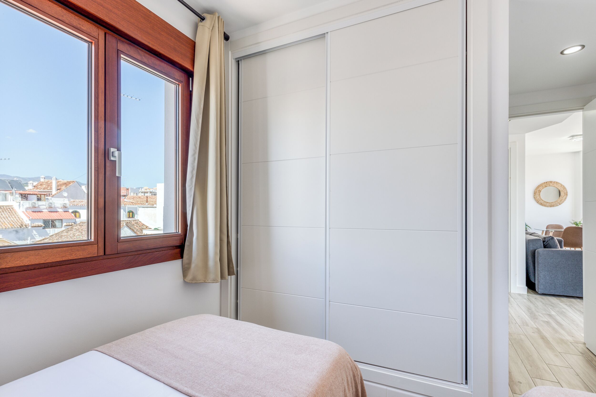 A bedroom with a large window, a sliding door, and a view of buildings outside.