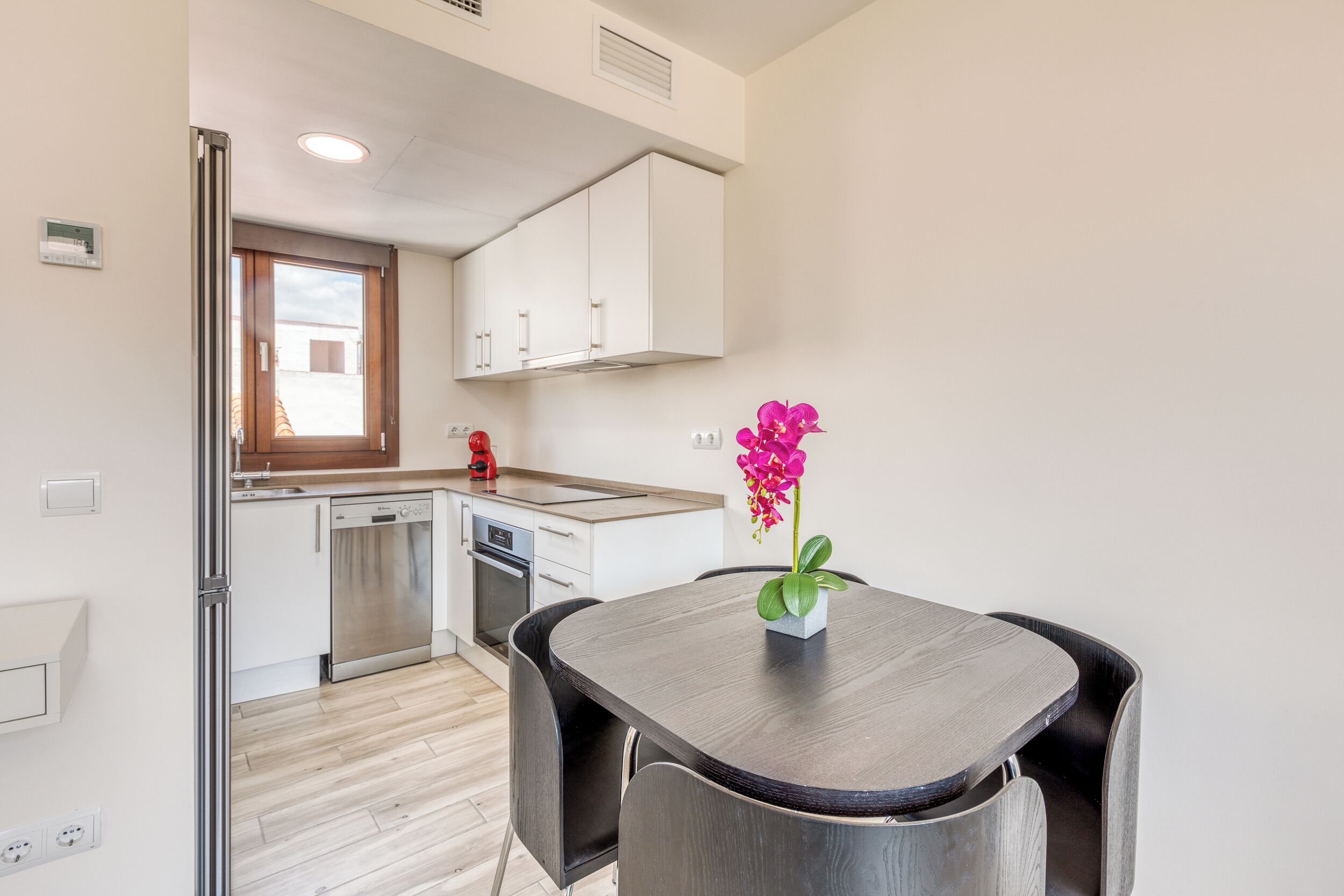 A modern kitchen with white cabinets, a stainless steel dishwasher, and a window above the sink.
