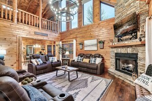 A log cabin interior with a fireplace, leather sofas, a dining area, and a balcony. - 4BR Cabin with Hot Tub, Game Room, & Pickle Ball! (Sevierville)
