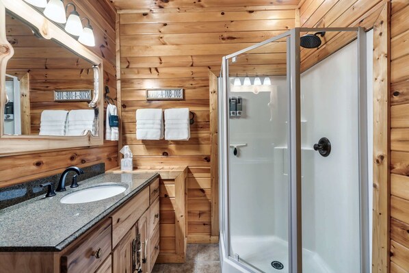 A wooden cabin bathroom with a sink, mirror, towel rack, and a glass-enclosed shower. - 4BR Cabin with Hot Tub, Game Room, & Pickle Ball! (Sevierville)