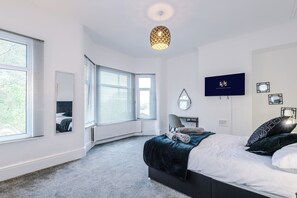 Relax in a serene bedroom with a large bed, flat-screen TV, and ceiling light fixture.