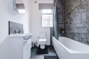 Features a sleek vanity, standalone toilet, and bathtub in a clean-lined space.