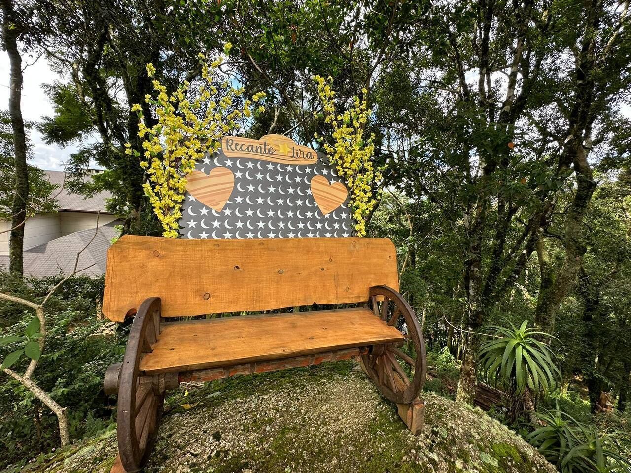A wooden bench with a sign that reads "Recanto da Lua" surrounded by trees and greenery.