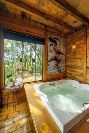 Eine Holzhütte mit einem großen Fenster, einer Whirlpool-Badewanne und einem kleinen Tisch mit Blumen.