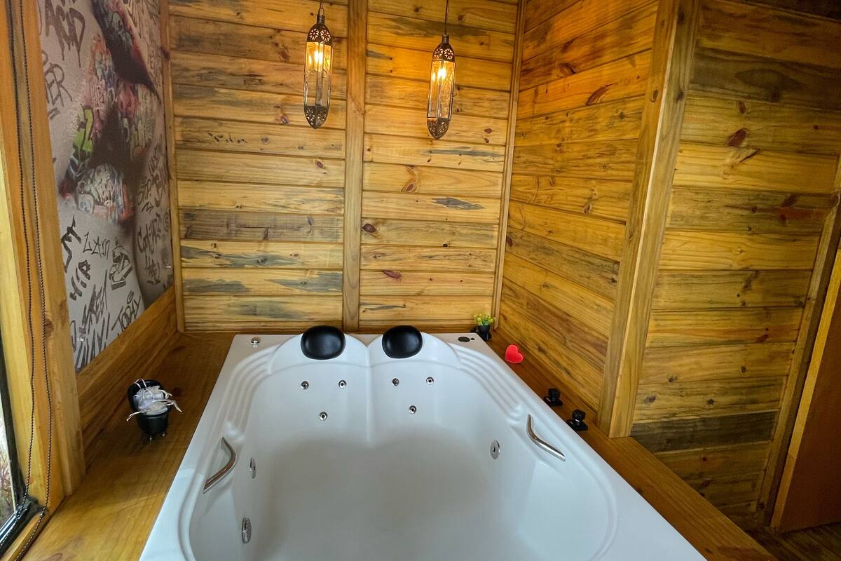 L’intérieur d’un chalet en bois, avec une grande baignoire, des murs en bois et deux luminaires suspendus.