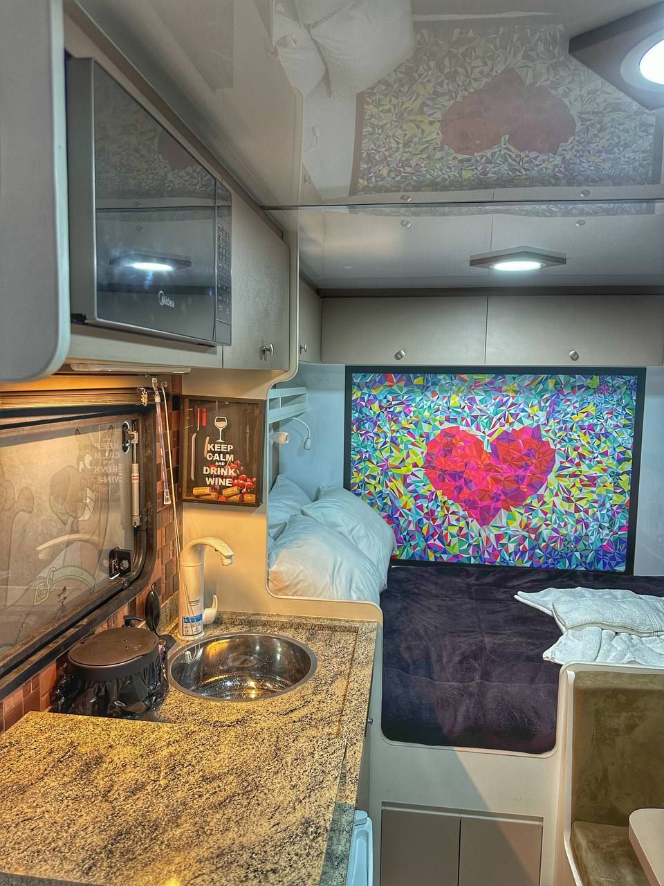 Un intérieur de camping-car compact comprenant un coin cuisine, un lit, une grande peinture abstraite et un petit bol pour chien.