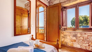 Un dormitorio con cama, un armario de madera, pared de piedra y balcón con vistas.