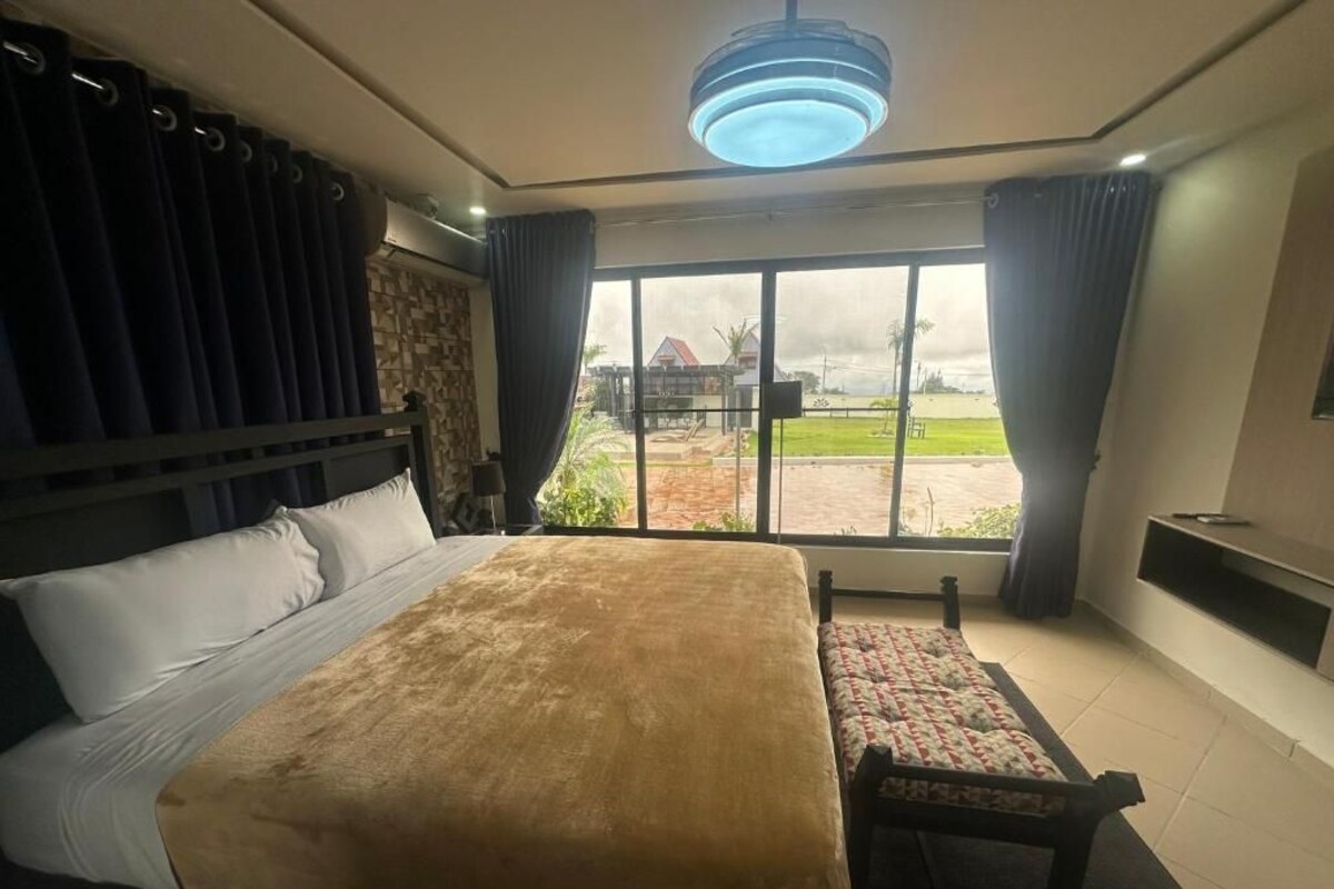 Ein Schlafzimmer mit einem großen Bett, einem Holzkopfende, einer Bank und Blick auf einen Innenhof durch eine Glastür.