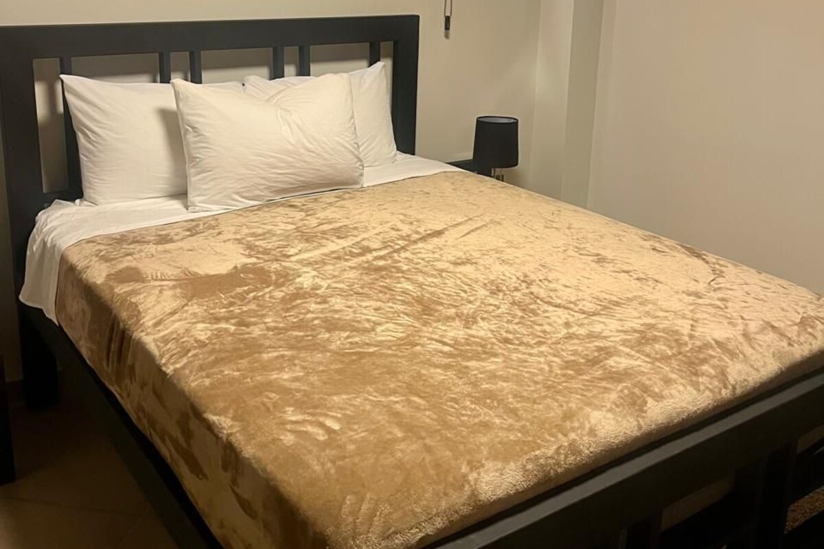 Ein Bett mit Kopfstütze, zwei Kissen und einer beigen Tagesdecke.
