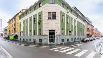 Ein Eckgebäude mit grüner Fassade, einem gut erkennbaren Eingang und einer Straßenszene mit parkenden Autos.