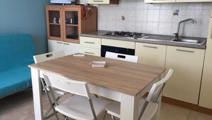 A compact kitchen with a wooden table and white chairs, a built-in stove, and a small cabinet with a television above it. - Apartment only 200mt from the beautiful beach Private parking (Torre San Giovanni)