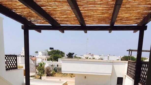 A covered outdoor seating area with a table and chairs, a small round table, and a view of the surrounding buildings. - Apartment only 200mt from the beautiful beach Private parking (Torre San Giovanni)