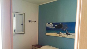A bedroom with a bed, a nightstand, a painting of a beach scene, and a mirror on the wall. - Apartment only 200mt from the beautiful beach Private parking (Torre San Giovanni)