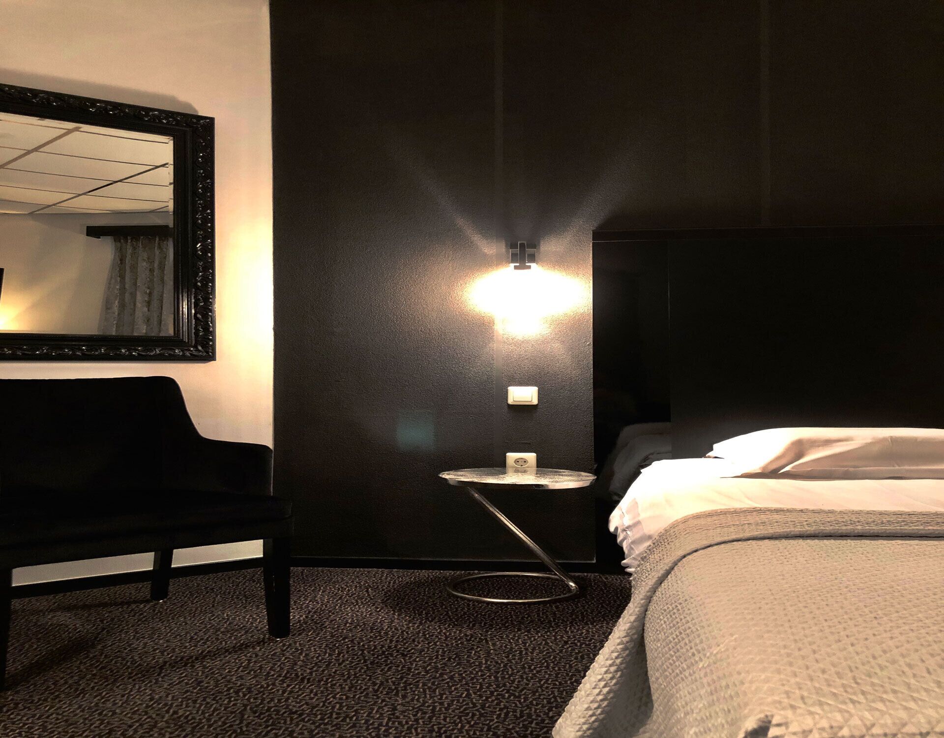 Ein Hotelzimmer mit Bett, einem Sessel, einem kleinen Tisch mit Lampe und einem wandmontierten Spiegel.