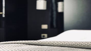 A close-up of a bed with a textured white cover, a dark wall with a white object on it, and a black object on the wall.