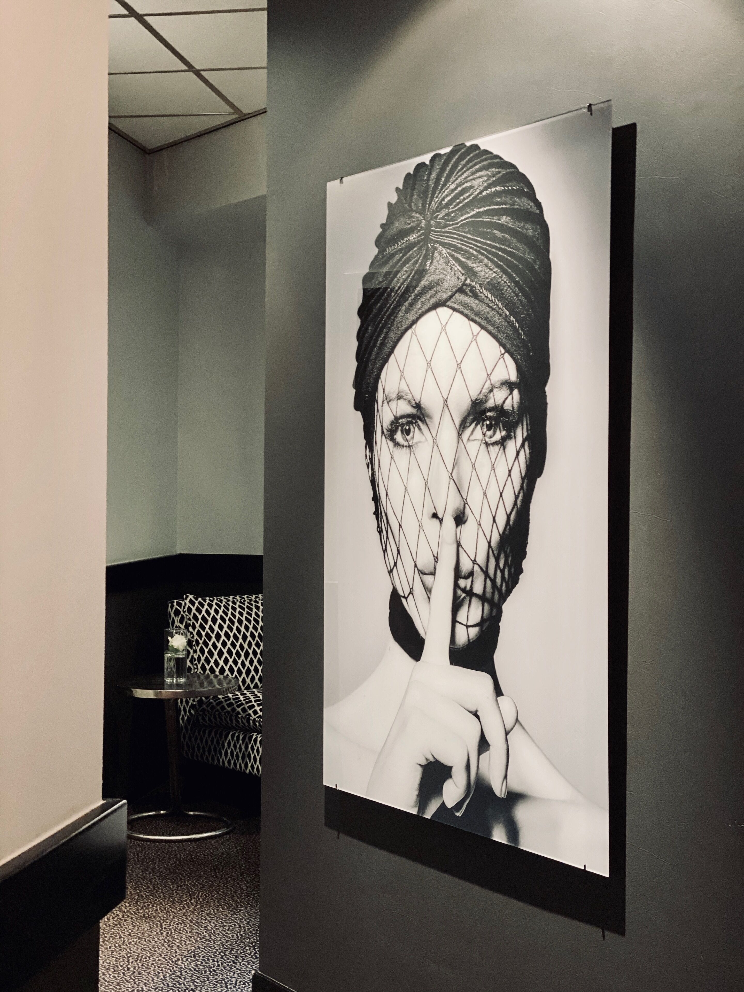 A black and white photograph of a person with a mesh veil, mounted on a wall in a room with a patterned sofa and a small round table.