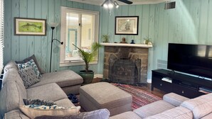 A living room with a sectional sofa, a fireplace, a television, and a ceiling fan. - North End Villa-behind the Cavalier2blocks2 beach (Virginia Beach)