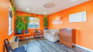A room with orange walls, a wooden floor, a sofa, a chair, a desk, and two potted plants. - Regency Inn By OYO Rockdale TX (Rockdale)
