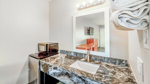 A bathroom with a marble sink, a vanity mirror with lights, and a towel rack. - Regency Inn By OYO Rockdale TX (Rockdale)