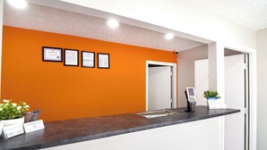 A reception desk with an orange wall, framed certificates, a digital kiosk, and a small plant. - Imperial Inn Tazewell (Tazewell)
