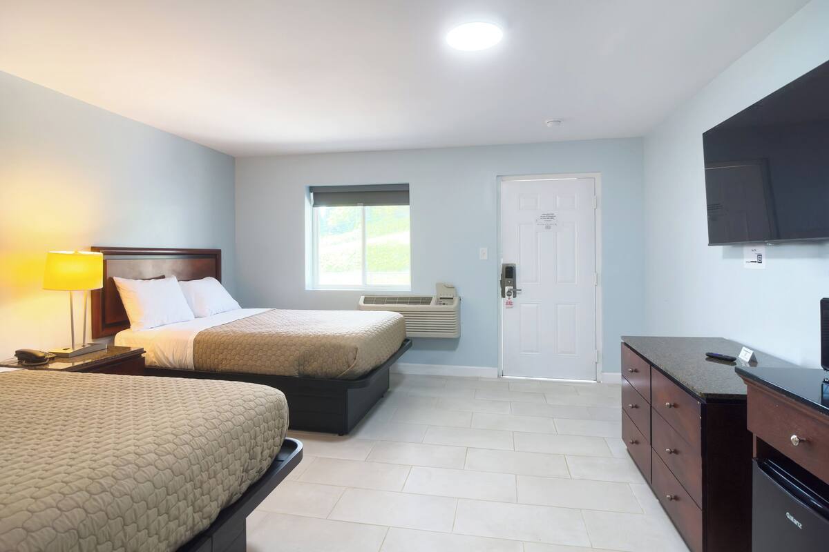 A hotel room with two beds, a TV, a desk, and a window.