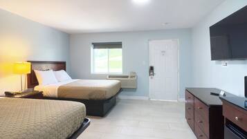 A hotel room with two beds, a TV, a desk, and a window.