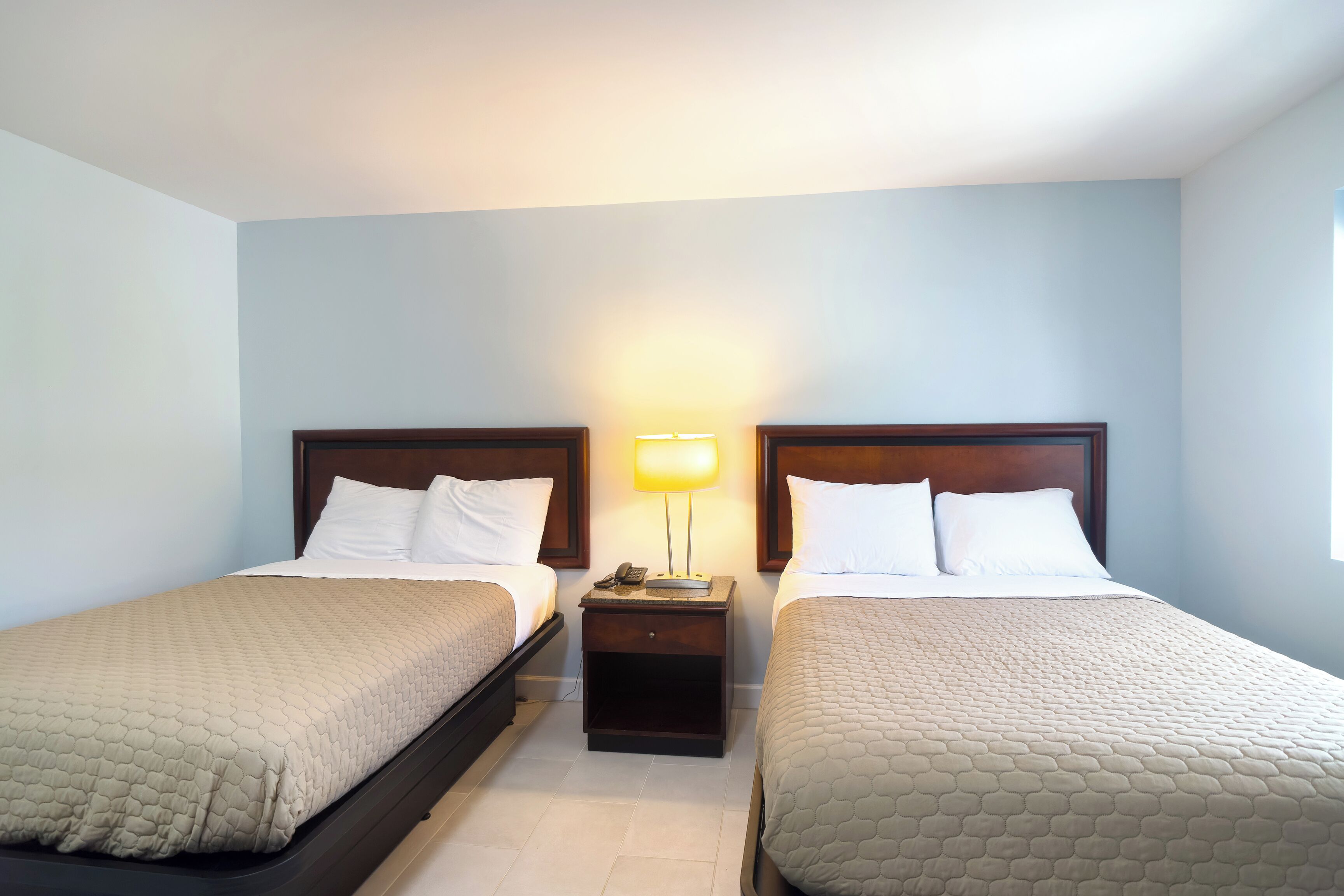A hotel room with two single beds, a nightstand with a lamp, and a window.