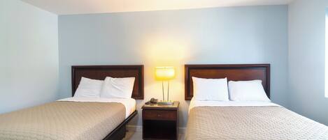 A hotel room with two single beds, a nightstand with a lamp, and a window.