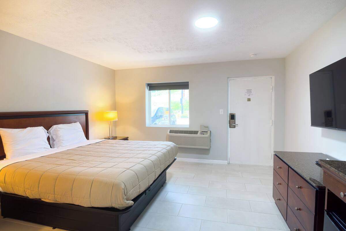 A bedroom with a bed, bedside lamp, air conditioning unit, and a TV on the wall.