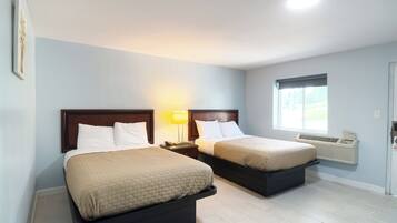 A hotel room with two beds, a nightstand with a lamp, a window with an air conditioner, and a door with a lock.