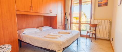 A bedroom with a bed, wooden wardrobe, and a view of the outside.