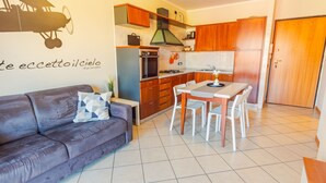 A compact kitchen with wooden cabinets, a built-in oven, and a dining area with a table and chairs. - Garden Residence - Italian Homing (Desenzano del Garda)