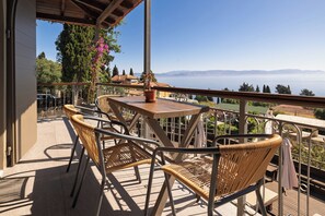 A balcony with wicker chairs and a table, overlooking a scenic view of mountains and a body of water. - Two-Bedroom Sea View Apartment with Communal Pool (Corfu)