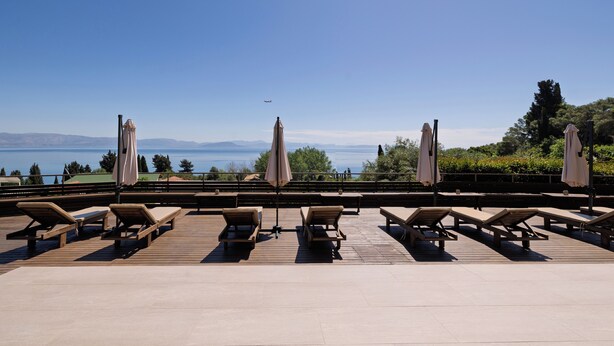 Une terrasse avec des chaises longues et des parasols, offrant une vue sur un plan d’eau et des montagnes.