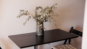 Une table à manger ornée d’un vase contenant des branches d’eucalyptus, deux chaises avec des sièges rembourrés et un plateau de table en bois foncé.